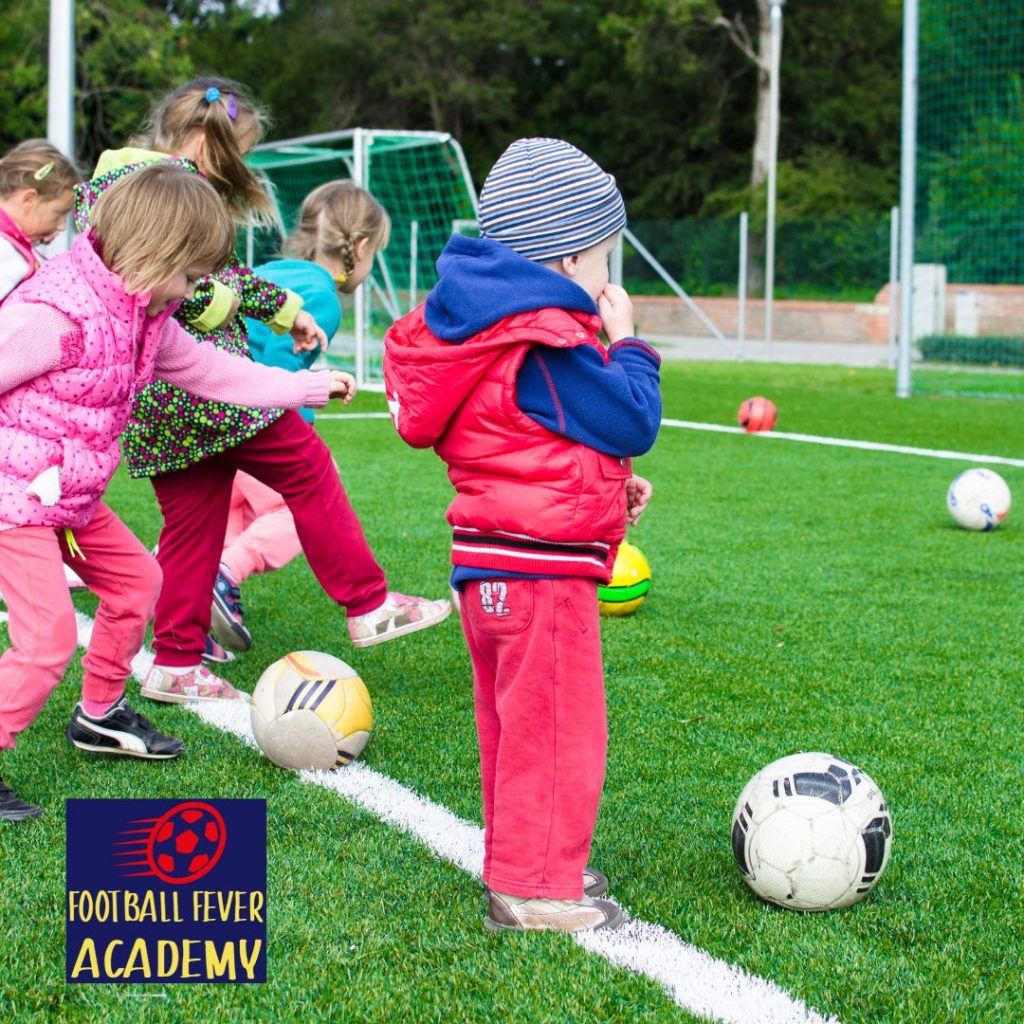 toddlers having fun on a football pitch with footballs